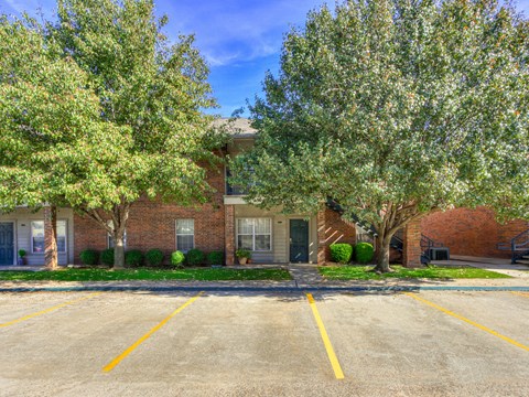 A parking lot in front of a brick building with trees on either side.