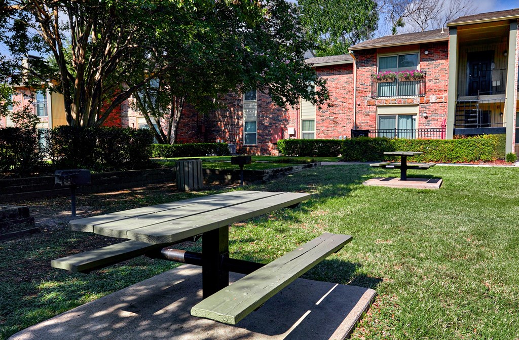 A large wooden table with two benches is in the foreground of a grassy area.