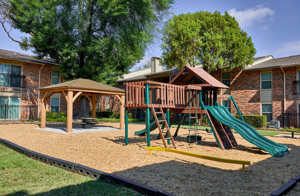 A playground with a green slide and a brown sandbox.