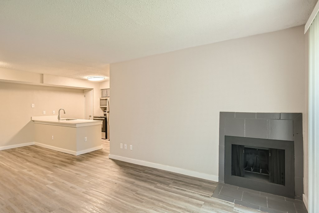 A modern living room with a fireplace and a kitchen area in the background.