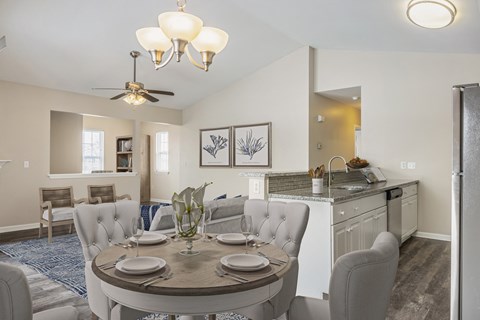 A dining room with a table set for two and a kitchen area in the background.