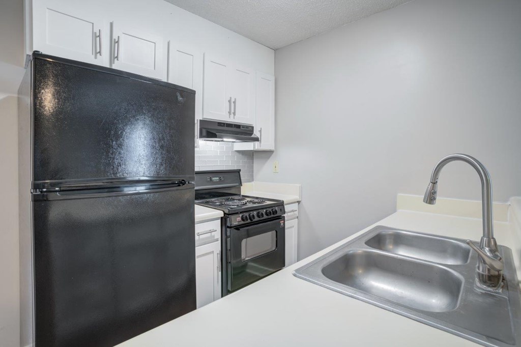 A black refrigerator sits next to a stove and oven in a kitchen.