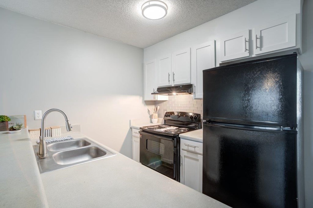 A black refrigerator sits in a kitchen with white cabinets.