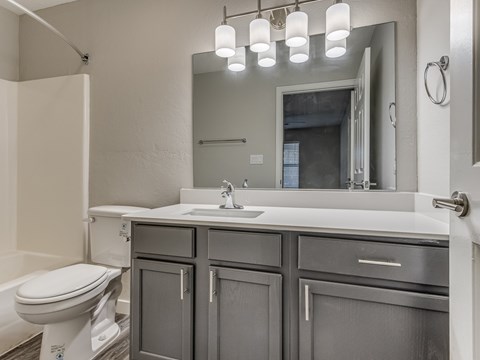 A bathroom with a white toilet, sink, and grey cabinets.