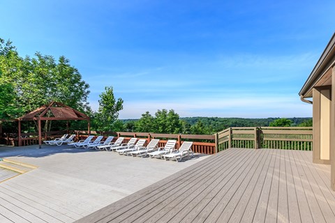 A wooden deck with chairs and a gazebo overlooking a forest.