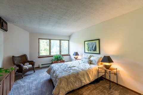 A bedroom with a bed, chair, and lamp.