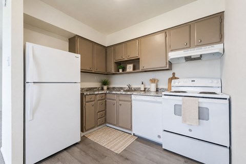A white refrigerator stands in a kitchen with brown cabinets and a white stove.