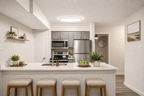 A kitchen with white cabinets and a white island with three stools.