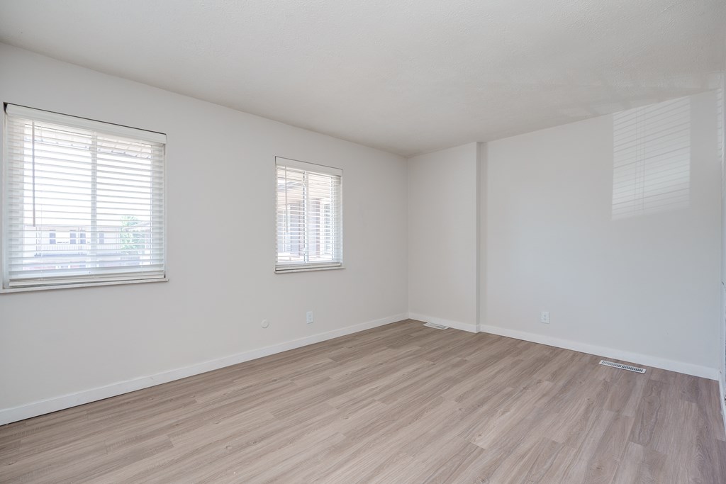 A room with wooden flooring and two windows.