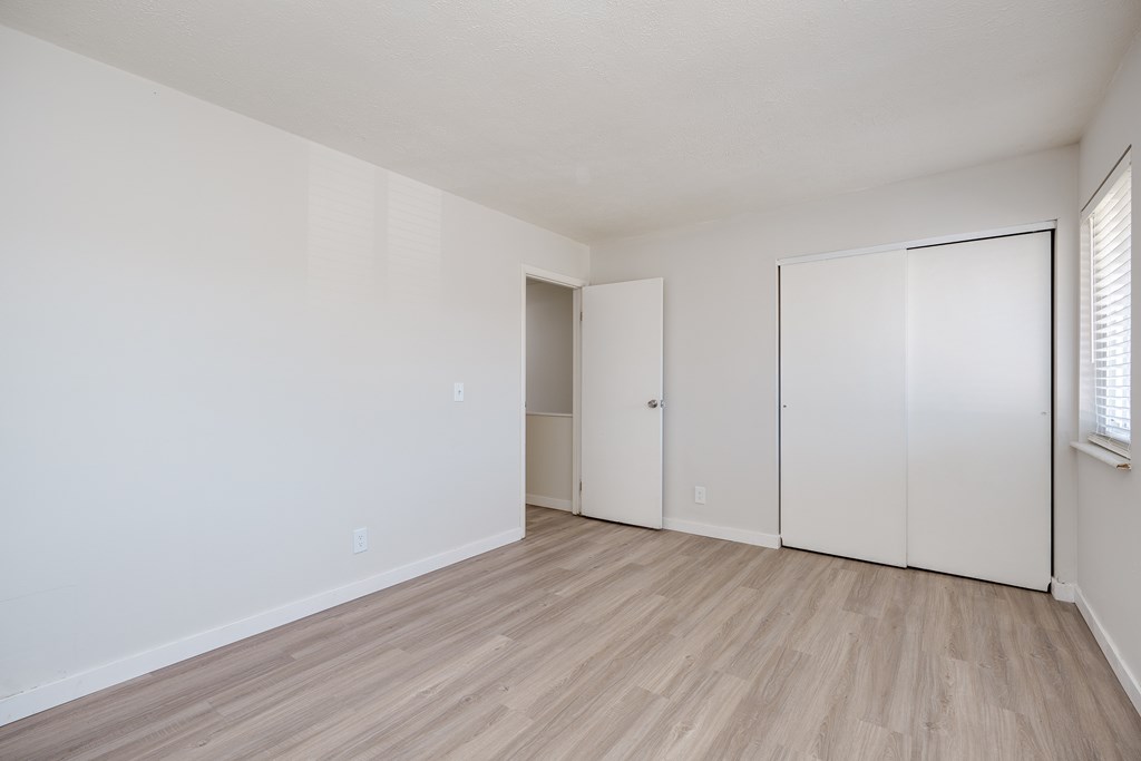 A room with white walls and wood flooring with a door on the left and a closet on the right.