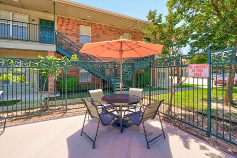 A patio with a table and chairs and an orange umbrella.