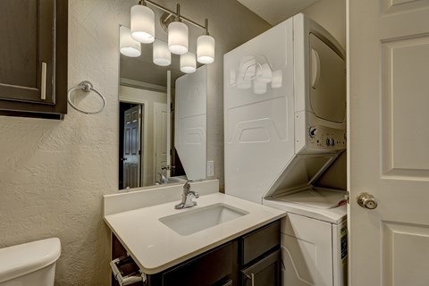 A bathroom with a sink, mirror, and a washer and dryer stacked in the doorway.
