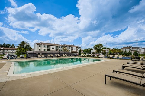 A large outdoor swimming pool with sun loungers and a building in the background.