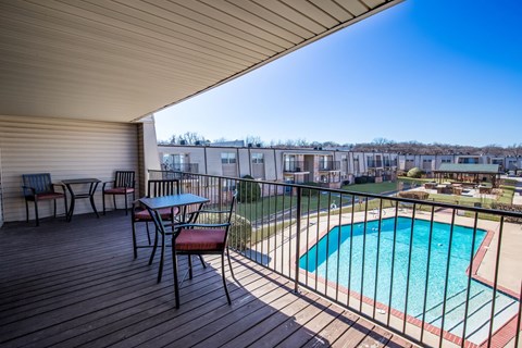 A wooden deck with a table and chairs overlooking a pool.