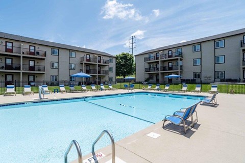 A swimming pool surrounded by lounge chairs and apartment buildings.