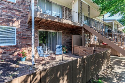 a patio with two chairs and a balcony in front of a brick house