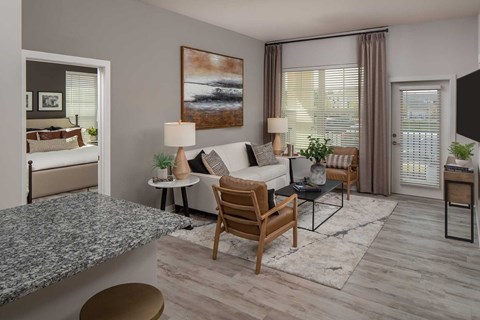 A living room with a grey sofa, a wooden chair, a grey table, a painting on the wall, and a window with curtains.