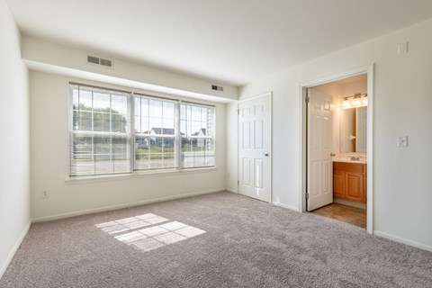 A spacious room with a large window and a door leading to another room.