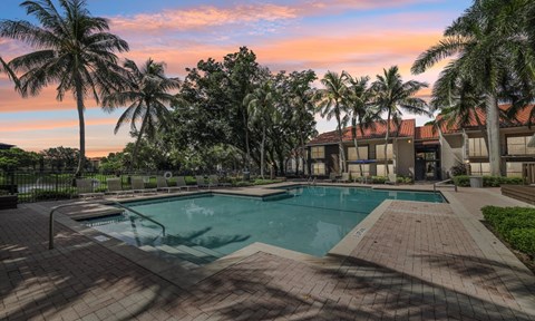 A swimming pool surrounded by palm trees and a building in the background.