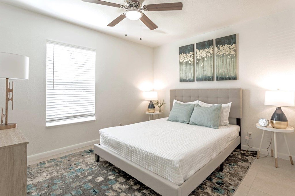 A bedroom with a large bed, a ceiling fan, and a window with blinds.