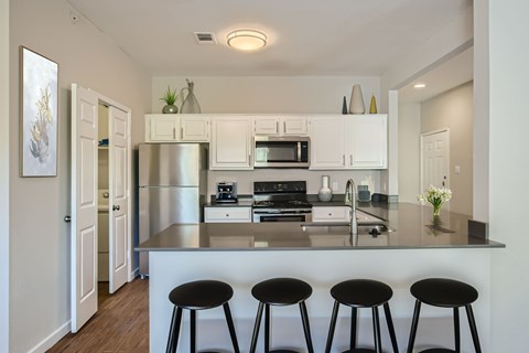 A modern kitchen with white cabinets and black stools.