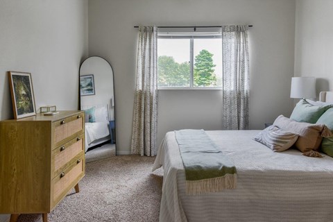 A bedroom with a bed, nightstand, and window with curtains.