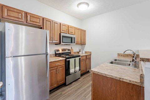 A kitchen with a refrigerator, microwave, oven, and sink.