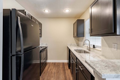 A kitchen with a black refrigerator and cabinets.
