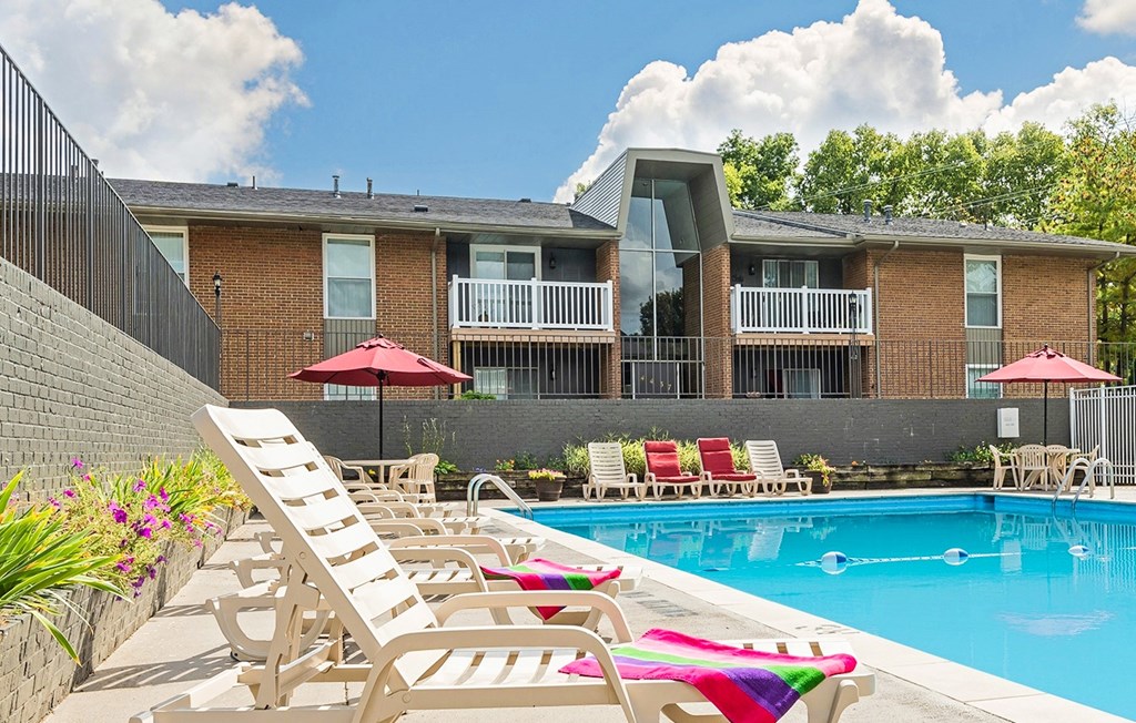 A pool with chairs and umbrellas in front of a building.