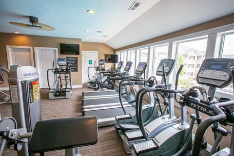 a gym with various cardio equipment and windows
