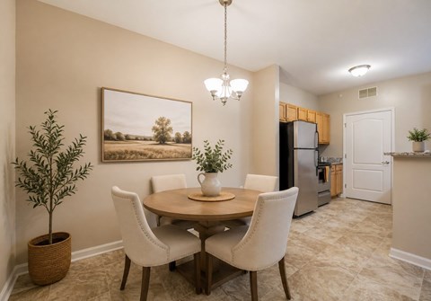 A dining room with a round table and chairs, a potted plant, and a painting on the wall.