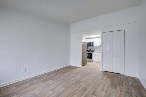 A room with a white door and a kitchen in the background.