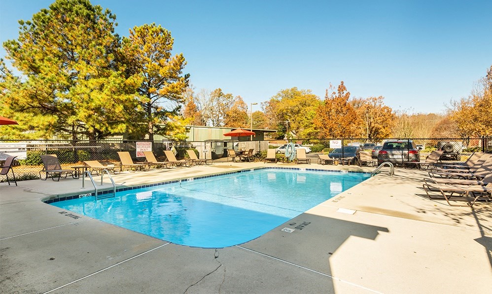 a swimming pool with chairs around it and trees in the background