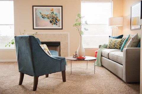 A living room with a blue chair, a white couch, and a painting on the wall.