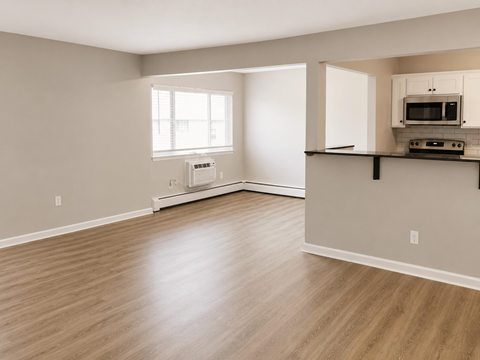 A spacious living room with a window, a microwave, and a wooden floor.