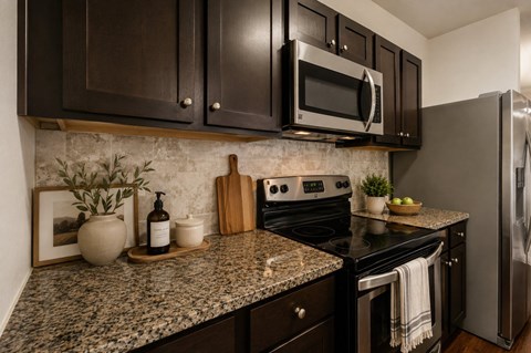 A kitchen with granite countertops and dark brown cabinets.