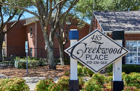 A sign for Creekwood Place stands in front of a brick building.