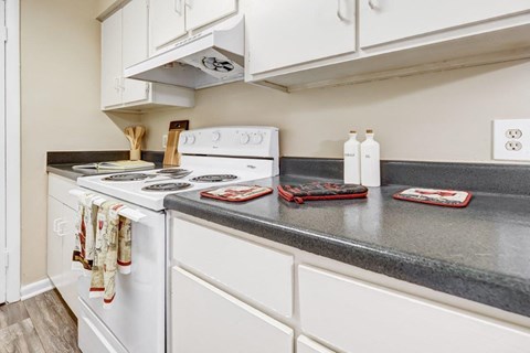 A kitchen with a white stove top oven and white cabinets.