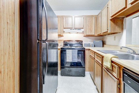 A kitchen with a black refrigerator and wooden cabinets.