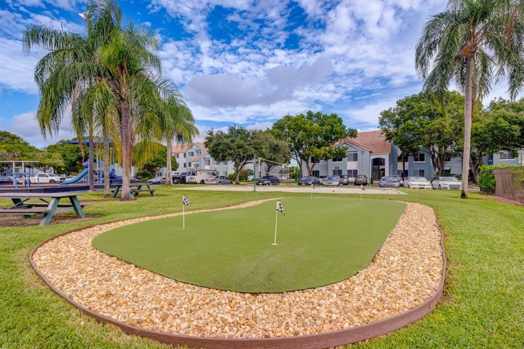 a putting green with palm trees and houses in the background