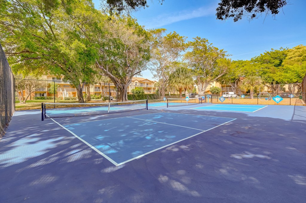 A tennis court surrounded by trees and a fence.