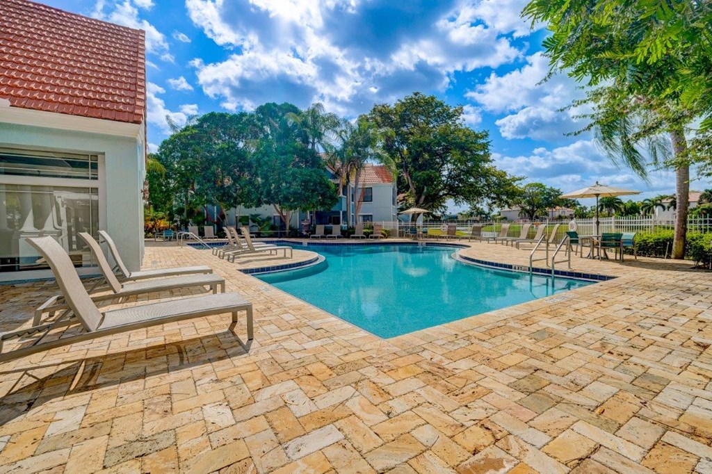 a swimming pool with lounge chairs and trees in the background