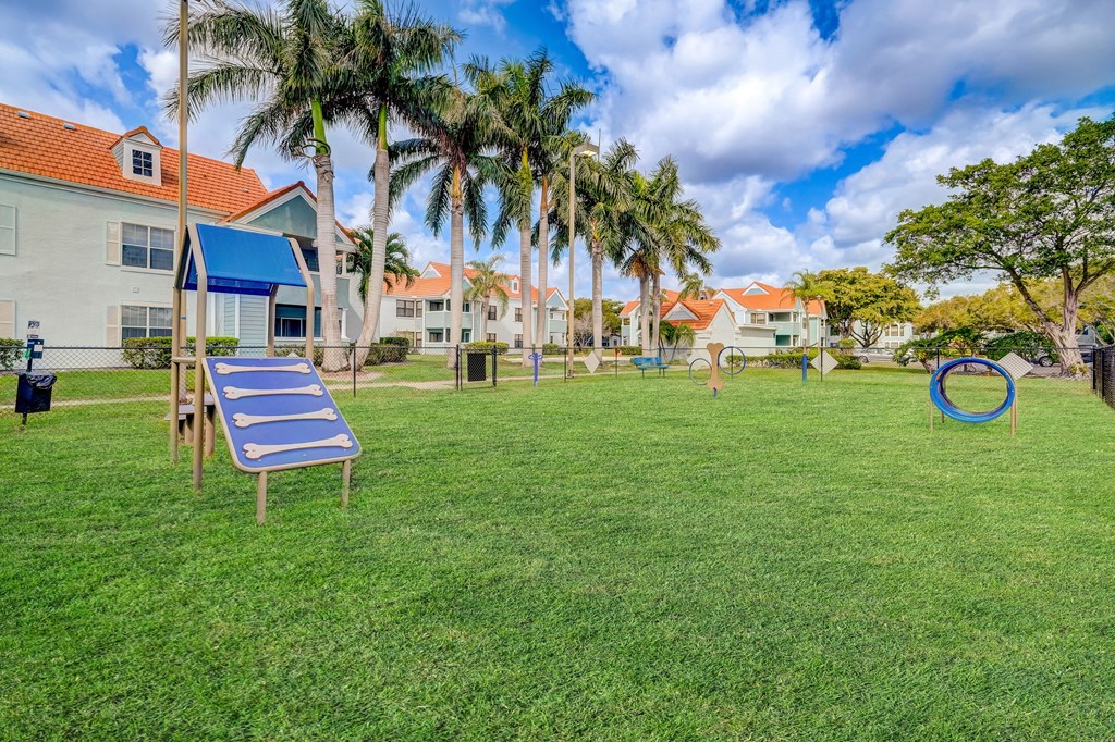 a grassy area with a trampoline and a trash can in front of a row