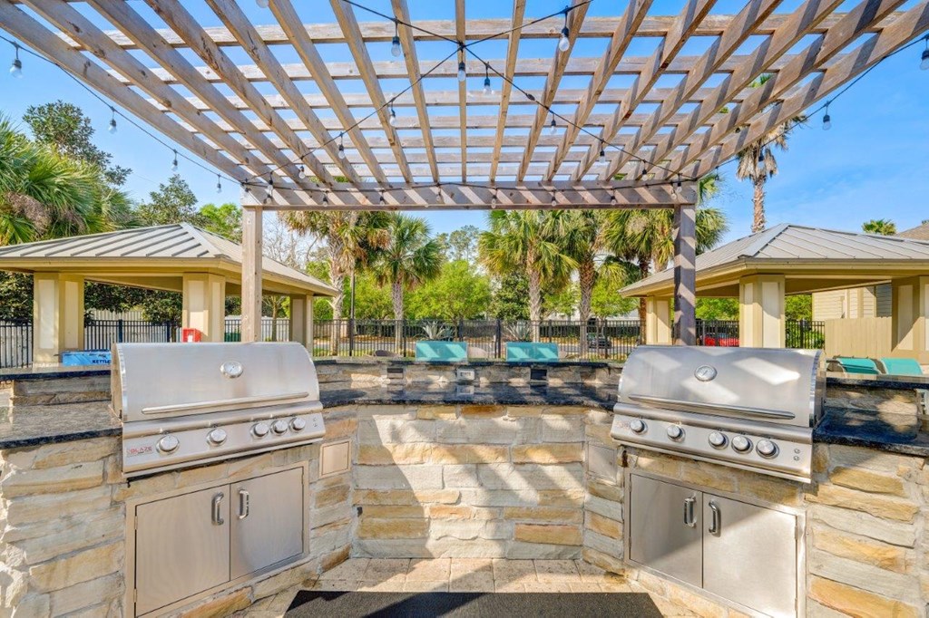 a pergola with two barbecue grills and a pool in the background
