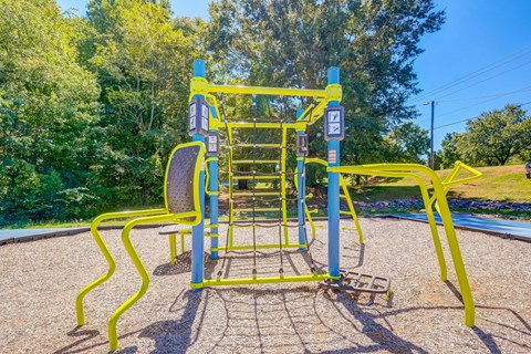 a yellow and blue playground with two chairs and trees in the background