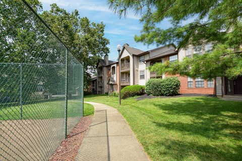 A green fence runs along a sidewalk in front of apartment buildings.