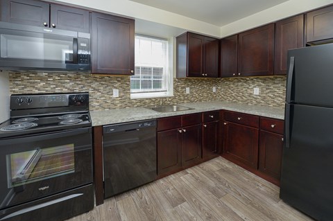 A kitchen with dark wood cabinets and a stone backsplash.