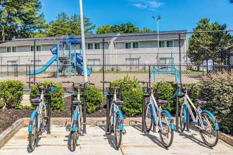 A row of bicycles are parked in front of a playground.