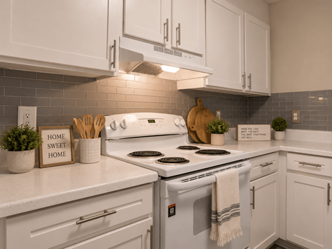 A kitchen with a white stove top oven and white cabinets.