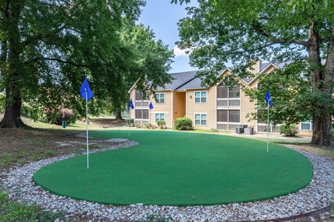 a putting green with blue flags in front of an apartment building
